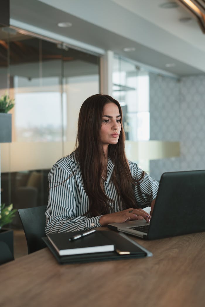 Focused businesswoman typing on laptop in a stylish, modern office setting.